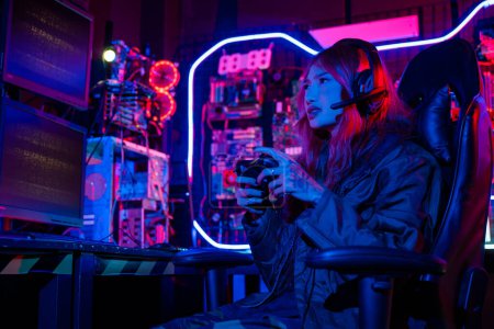 Foto de Mujer joven usa auriculares para juegos jugando juegos de esports sala de juegos de consola, Gamer usa controlador de joystick para juegos de torneos virtuales videojuegos en línea con luces de neón de computadora - Imagen libre de derechos