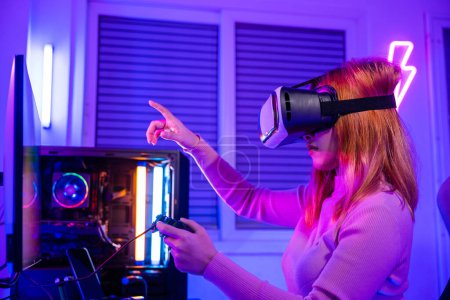 Foto de Gamer in VR headset glasses exploring metaverse plays online video game touching something on air with neon lights, Excited woman playing watching video life simulation at home - Imagen libre de derechos
