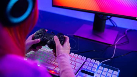 Gamer using joystick controller for virtual tournament plays online video game with computer neon lights, woman wear gaming headphones playing live stream esports games console at home