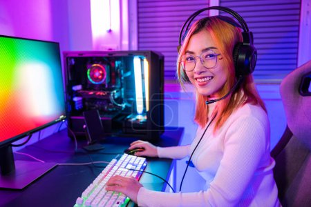 Foto de Happy Gamer endeavor plays online video games tournament with computer neon light, Smiling young woman wearing gaming headphones intend to do playing live stream games online at home looking to camera - Imagen libre de derechos