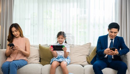 Photo for Family dont care about each other. Asian parents ignore their child and looking at their mobile phone at home, gadgets dependence overuse internet social media addiction on sofa living room - Royalty Free Image