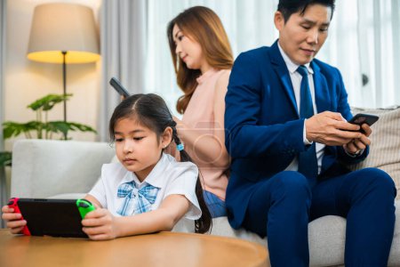 Foto de La familia no se preocupa por los demás. Los padres asiáticos ignoran a sus hijos y mirando su teléfono móvil en casa, la dependencia de los gadgets abusa de la adicción a las redes sociales en el sofá sala de estar - Imagen libre de derechos