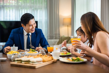 Foto de Asian family father, mother with children daughter eating healthy breakfast food on dining table kitchen in mornings together at home before father left for work, happy couple adult family concept - Imagen libre de derechos