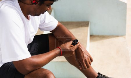 Photo for Close up Asian young athlete sport runner black man wear modern time smart watch he sitting resting before training running at the outdoor street health park, healthy exercise before workout concept - Royalty Free Image