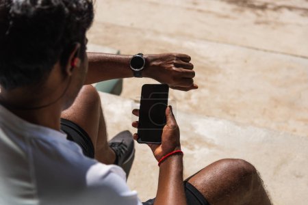 Téléchargez les photos : Fermer Asiatique jeune athlète sportif coureur homme noir porter moderne montre intelligente temps et synchroniser avec un smartphone vérifier le résultat de course après une course d'entraînement à l'extérieur, la technologie d'entraînement sain - en image libre de droit