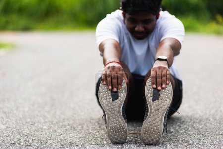 Téléchargez les photos : Gros plan Asiatique jeune athlète sport coureur noir homme porter montre il assis tirer orteil pieds étirant les jambes et le genou avant de courir au parc de santé de rue en plein air, exercice sain avant concept d'entraînement - en image libre de droit