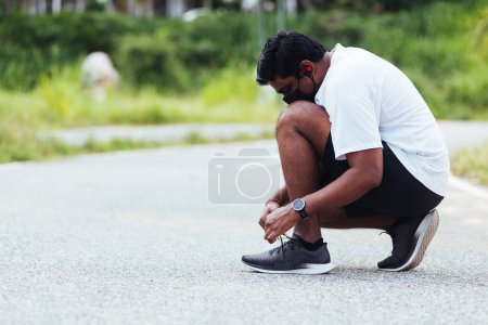 Téléchargez les photos : Gros plan asiatique coureur de sport noir homme porter montre assis il essayer chaussures de course lacet se préparer pour le jogging et courir au parc de santé de la rue en plein air, concept d'entraînement d'exercice sain - en image libre de droit