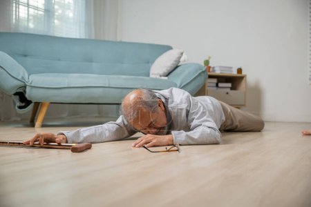 Téléchargez les photos : Homme âgé maux de tête couché sur le sol après être tombé il douleur et mal de l'ostéoporose, Homme âgé tombant sur le sol seul avec bâton de marche à la maison, Soins de santé et médicaments - en image libre de droit