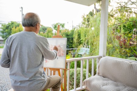 Téléchargez les photos : Lifestyle personnes âgées sourient peinture à son chevalet à l'extérieur de la maison, asiatique senior vieil homme peinture tableau à l'aide de pinceau et de couleur à l'huile sur toile, Happy Retirez artiste et concept d'activité - en image libre de droit