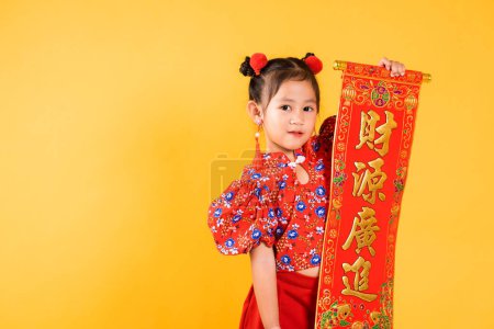 Téléchargez les photos : Nouvel An chinois. heureux asiatique chinois petit enfant fille sourire portant rouge cheongsam qipao printemps festival couplets caractère FU signifie fortune, bénédiction, studio tourné isolé sur fond jaune - en image libre de droit