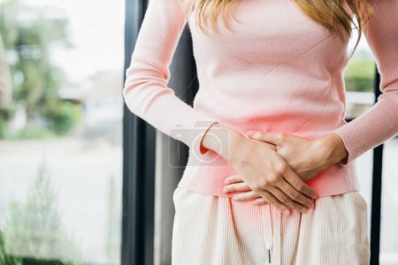 Asian young female unhappy unwell sick ill hand holding on stomach suffers pain at home, Sad Woman Stomach Ache from menstruation, Abdomen bloating and Chronic gastritis concept
