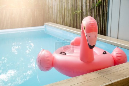 Téléchargez les photos : Pink inflatable ring flamingo plastic in the swimming pool blue water, Pool accessory equipment float for party, Trendy summer vacation feeling concept - en image libre de droit