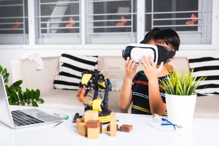 Téléchargez les photos : Virtual Reality Simulator. Asian kid boy using VR glasses on robotic arm in workshop, Child learning programer control robot arm with sensors to pick up wood block, Technology education. industry 4.0 - en image libre de droit