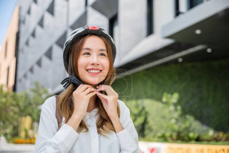 Téléchargez les photos : Asiatique jeune femme d'affaires mettant casque de vélo préparé cyclistes autour de la construction aller au travail, Gros plan femme souriante portant casque exercice à l'extérieur avec vélo dans la rue, Transport Économisez de l'énergie - en image libre de droit