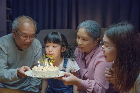 Foto de Feliz familia asiática abuelos y madre celebrando disfrutar de fiesta de cumpleaños con pastel de nieta Soplando vela en casa en la noche, concepto de sorpresa de cumpleaños - Imagen libre de derechos
