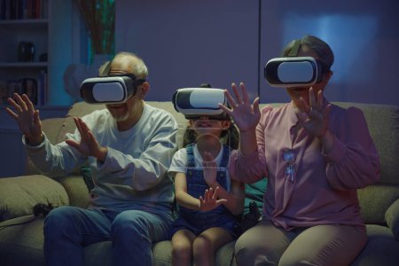 Téléchargez les photos : Aînés asiatiques avec enfant jouer VR jeu vidéo, divertissement familial, petite-fille et grands-parents jouer ensemble passionnants jeux vidéo intéressants en utilisant des casques de réalité virtuelle salon à la maison - en image libre de droit