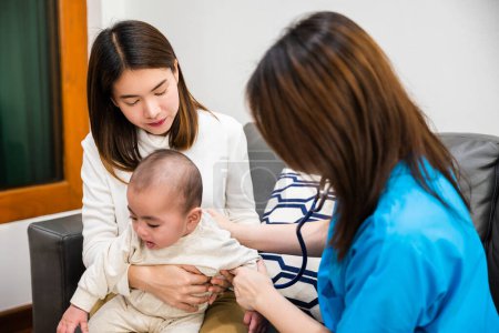 Foto de La madre asiática trajo al bebé para ver al médico y al médico comprobó la fiebre, el pediatra examinó al bebé recién nacido con el padre de la mujer, el cuidado de la salud y el concepto médico - Imagen libre de derechos