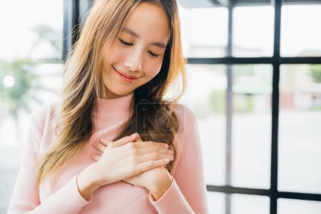 Photo for Beauty Asian young woman touching her chest for thanking at home, happy charming female smiling hold hands chest near heart honest with grateful gesture - Royalty Free Image