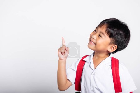 Photo for Asian toddler smiling happy wear student thai uniform red pants keeps pointing finger at copy space in studio shot isolated on white background, Portrait little children boy preschool, Back to school - Royalty Free Image