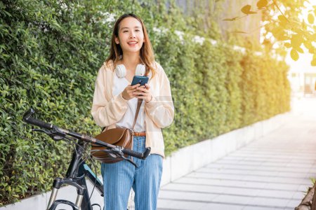 Photo pour Asiatique jeune femme commuer sur smartphone avec vélo en été dans le parc campagne en plein air, Happy femelle sourire marcher dans la rue avec son vélo sur la route de la ville et téléphone portable avec téléphone portable - image libre de droit