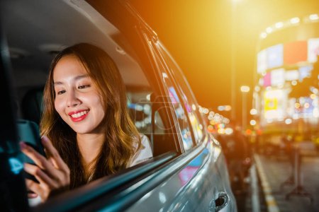 Foto de Asian businesswoman working late commuting from office in Taxi backseat with mobile phone in city at night after late work, Happy beautiful woman texting smartphone sitting car back seat in urban - Imagen libre de derechos