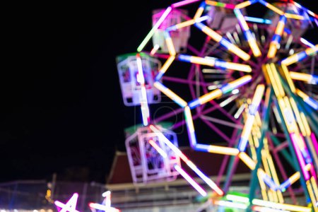 Photo for Blurry rollercoaster in bokeh, Ferris wheel at night of colorful with outdoor, Defocused blurred and blur image of Amusement park, The annual temple event has activities. Image out of focus - Royalty Free Image