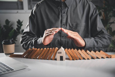 Photo for Business risk plan real estate protection. Man hand blocks wood block from many row falling wooden block like domino to house model, Insurance ideas to prevent loss concept - Royalty Free Image