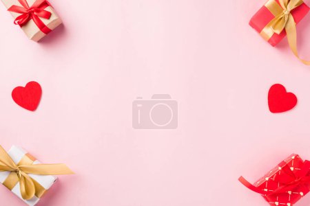 Photo for Valentines day background. Frame made of red gift box with ribbon bow and wood red hearts shaped composition greeting card for love isolated on pink background with copy space. Top View from above - Royalty Free Image