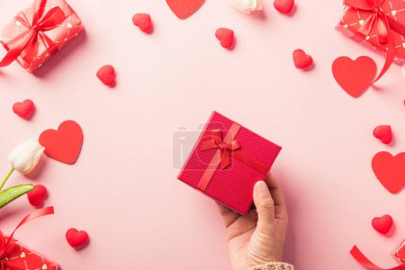 Foto de Día de San Valentín y cumpleaños. Manos de mujer sosteniendo regalo o regalo caja decorada y corazón rojo sorpresa sobre fondo rosa, paquete de caja de regalo de mano hembras en papel artesanal Vista superior plana lay - Imagen libre de derechos