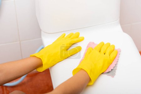 Photo for Woman cleaning toilet seat by pink cloth wipe restroom, female wearing yellow rubber gloves she sitting and clean the bathroom, Housekeeper healthcare concept - Royalty Free Image