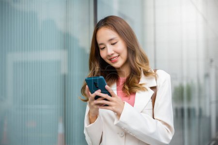 Photo for Happy business woman smiling using mobile phone outdoor walking on city street urban, Asian businesswoman texting smartphone commuting work she walking near her office building in morning - Royalty Free Image