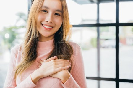 Photo for Happy charming female smiling hold hands chest near heart honest with grateful gesture, Beauty Asian young woman touching her chest for thanking feeling no stress at home, peace of mind concept - Royalty Free Image