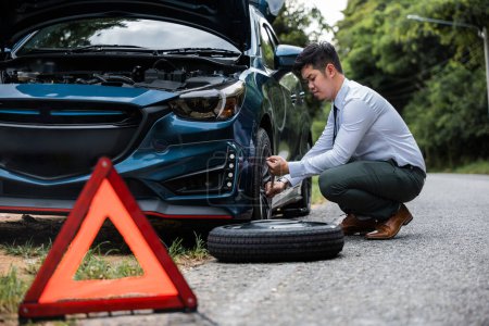Photo for Asian businessman car broken has problems with wheel of his car during go to work in morning he changing replace rubber tire on wheels, business man have warning sign on road, problem transportation - Royalty Free Image