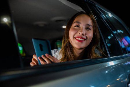 Photo for Happy beautiful woman texting smartphone sitting car back seat in urban, Asian businesswoman working late commuting from office in Taxi backseat with mobile phone in city at night after late work - Royalty Free Image