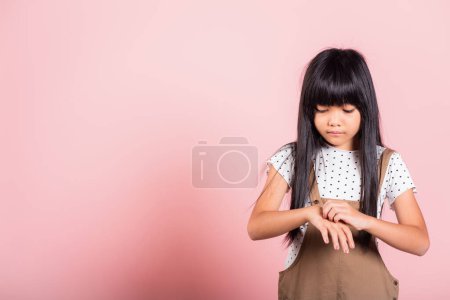 Foto de Asiático niño pequeño 10 años de edad rascarse la mano de nuevo picazón de mosquito picadura en el estudio tiro aislado sobre fondo rosa, niña dermatitis y sarna, síntomas de alergia, atención médica y medicina - Imagen libre de derechos
