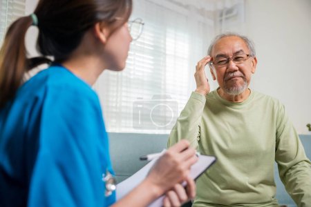 Asiatische ältere Männer Patienten haben Kopfschmerzen und Krankenschwester sprechen, überprüfen und Aufzeichnung der aktuellen Symptome auf Klemmbrett im Wohnzimmer, Home Healthcare und medizinischen Dienst