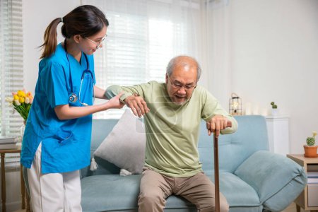 Téléchargez les photos : Infirmière soignante aidant un homme handicapé âgé à se lever avec un bâton de marche, une jeune femme aide les patients orthopédiques à se lever avec une canne à pied à la maison, Journée internationale des personnes âgées - en image libre de droit