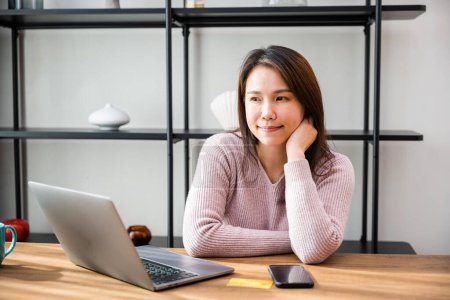 Foto de Dreamy mujer de negocios asiática que toma una decisión seria que trabaja en el ordenador portátil, mujer de negocios sentada en el escritorio de trabajo en la oficina pensando en la nueva estrategia de proyecto o vacaciones - Imagen libre de derechos