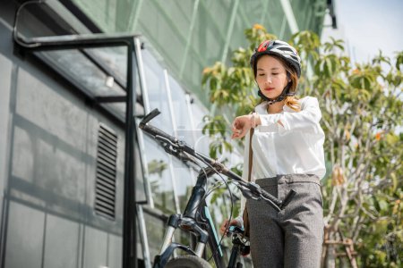 Téléchargez les photos : Portrait femme souriante vérifier montre, Asiatique jeune femme d'affaires debout avec vélo vérifier horloge heure sur la rue de la ville urbaine le matin aller au travail au bureau, Transport de banlieue d'affaires - en image libre de droit