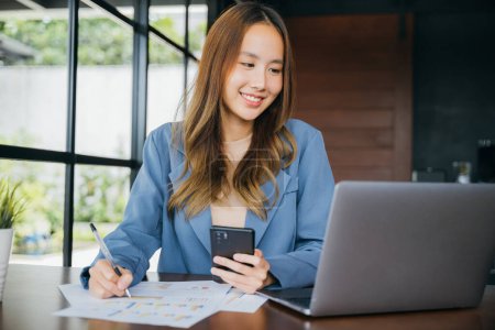 Foto de Mujer de negocios asiática sentada en cafés con teléfono inteligente móvil que escribe nota en gráfico gráfico gráfico de papeleo, contabilidad financiera femenina con gráfico de estadísticas de crecimiento y gráfico - Imagen libre de derechos