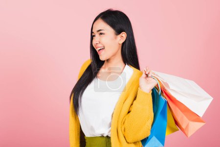 Téléchargez les photos : Portrait d'Asiatique heureux belle jeune femme adolescent shopper souriant debout excité tenant sacs à provisions en ligne multicolore coloré en été, prise de vue en studio isolé sur fond rose avec espace de copie - en image libre de droit