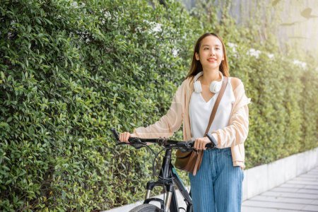 Téléchargez les photos : Heureuse femme souriante marcher dans la rue avec son vélo sur la route de la ville, environnement ECO, Voyage de vacances en bonne santé, Asiatique jeune femme marchant aux côtés de vélo en été dans le parc campagne en plein air - en image libre de droit
