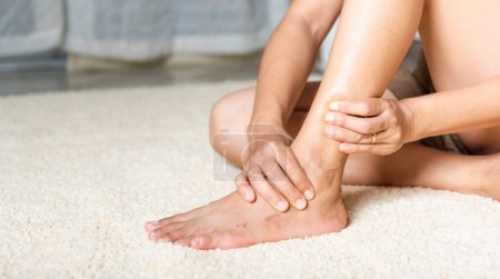 Photo for Foot pain, Woman holds her ankle injury feeling pain in her foot at home, female suffering from feet ache use hand massage relax muscle from ankle in home interior, Healthcare problems and medical - Royalty Free Image