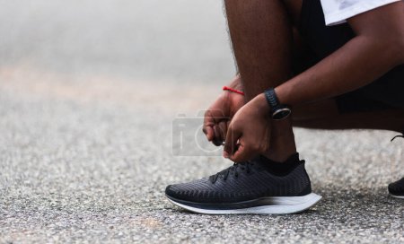 Téléchargez les photos : Gros plan asiatique coureur de sport noir homme porter montre assis il essayer chaussures de course lacet se préparer pour le jogging et courir au parc de santé de la rue en plein air, concept d'entraînement d'exercice sain - en image libre de droit