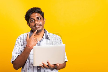 Photo for Closeup Asian happy portrait young black man holds a laptop computer hand finger handle on the chin and thinking question looking away, studio isolated on yellow background - Royalty Free Image