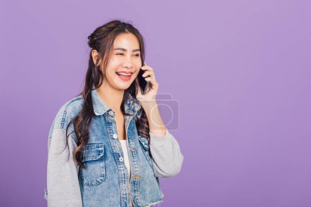 Téléchargez les photos : .Portrait d'Asiatique belle jeune femme confiante souriant sur appel téléphonique avec smartphone, Joyeux style de vie adolescent féminin appelant et parlant à ses amis, studio tourné isolé sur fond violet - en image libre de droit