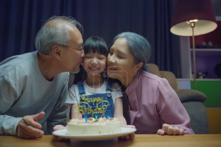 Téléchargez les photos : Joyeux anniversaire. Asiatique famille grand-père et grand-mère embrassé petite-fille se sentir reconnaissant tout en célébrant son anniversaire après avoir donné gâteau merveilleux, fête de famille senior avec enfant à la maison - en image libre de droit