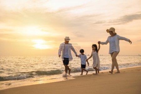 Téléchargez les photos : Famille heureuse qui s'amuse à courir sur une plage de sable au coucher du soleil, parents actifs et personnes père, mère, enfants fils et fille se tenant la main sur la plage, vacances d'été tropicales - en image libre de droit