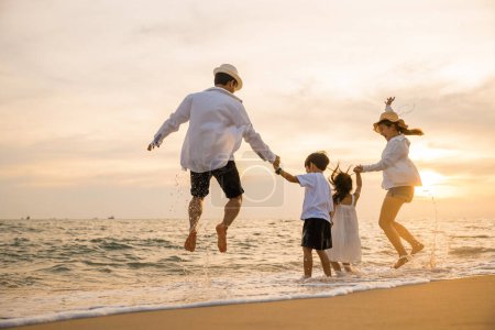 Téléchargez les photos : Heureuse famille asiatique ont plaisir à sauter ensemble sur la plage en vacances au coucher du soleil, Silhouette de la famille tenant la main vivre un mode de vie sain sur la plage, les gens de retour profiter de Voyage et concept de vacances - en image libre de droit