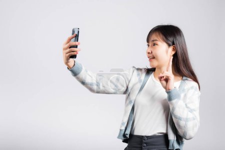 Foto de Mujer emocionada sosteniendo el teléfono inteligente para disparar foto selfie estudio de cámara frontal disparó fondo blanco aislado, feliz joven mujer sonriendo tomando fotografía por teléfono móvil en el teléfono móvil - Imagen libre de derechos